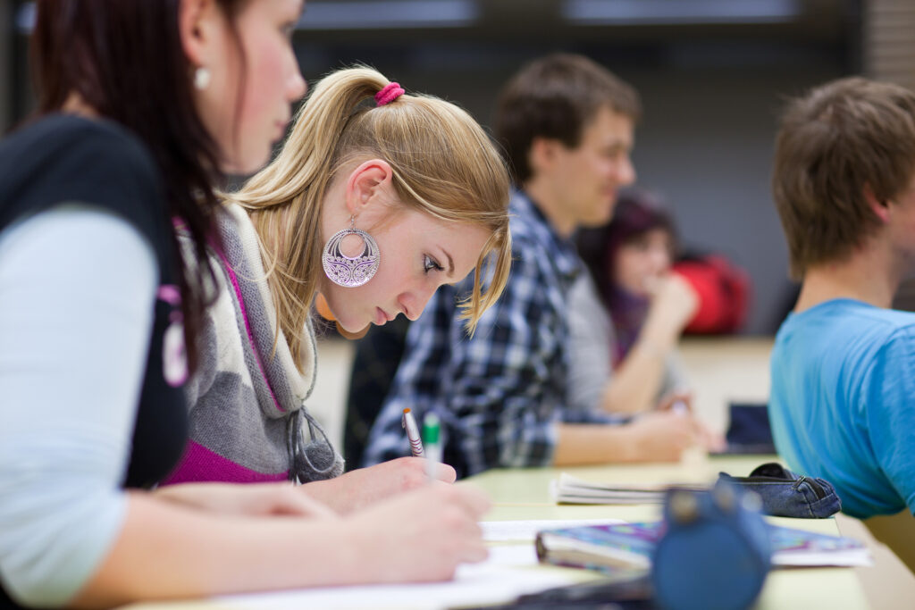 pretty female college student sitting in a classroom full of students during class (shallow DOF; color toned image)