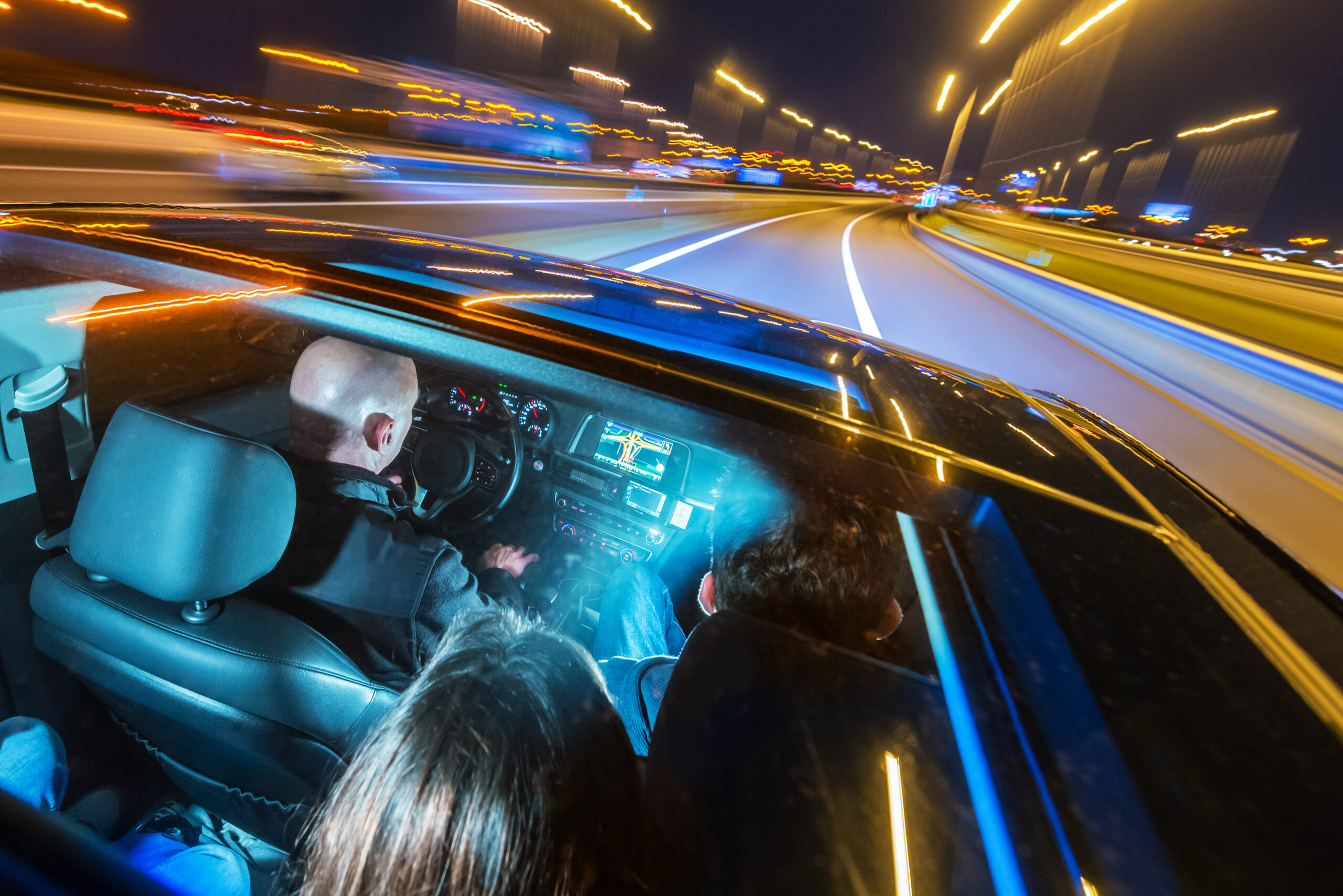Car pooling and mobility concept, shown by a full passengers car Car pooling and mobility concept, shown by a full passengers car sharing a ride, seen from the roof, through the sun roof at night, entering a motorway.