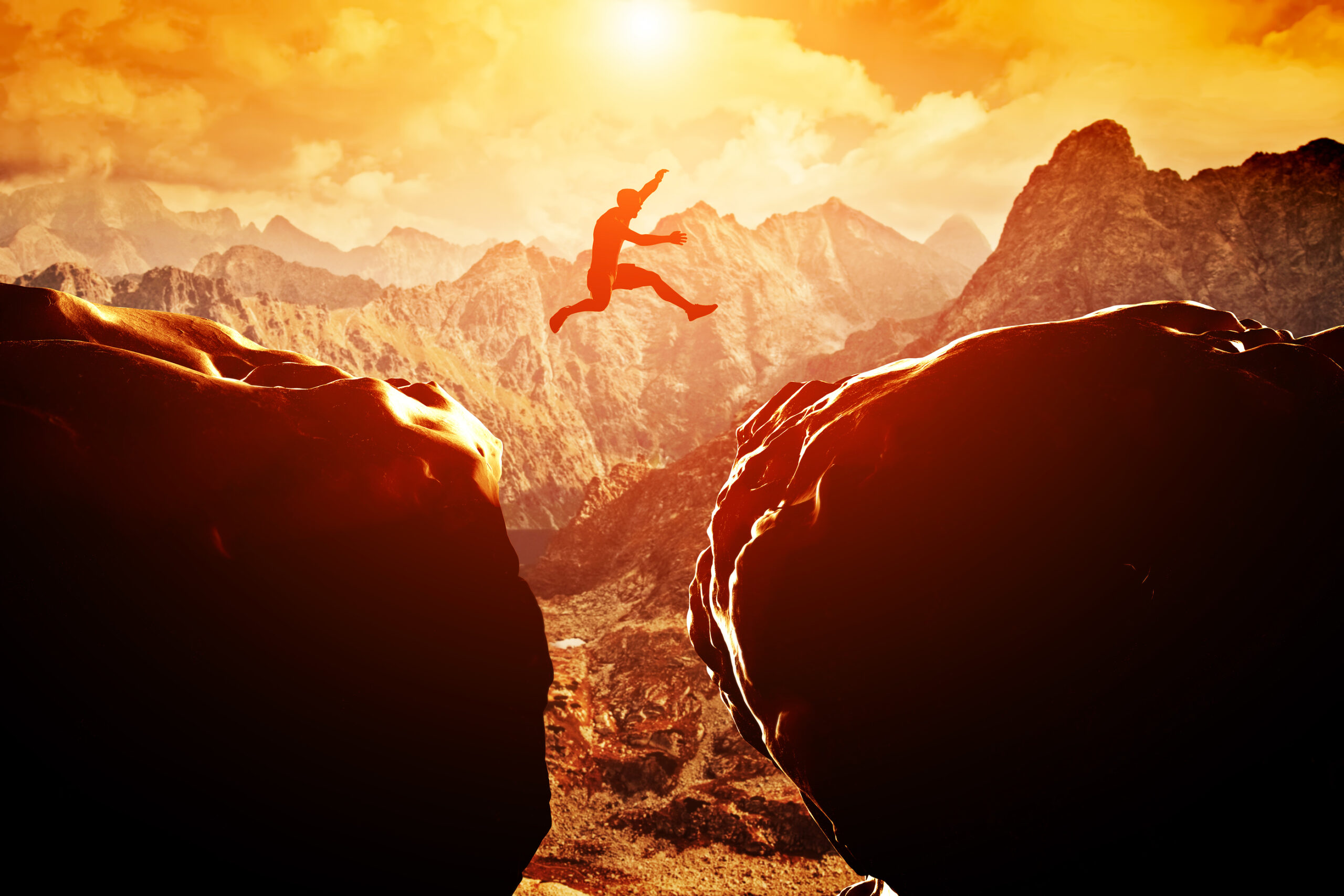Man jumping over precipice between two rocky mountains at sunset Man jumping over precipice between two rocky mountains at sunset. Freedom, risk, challenge, success.