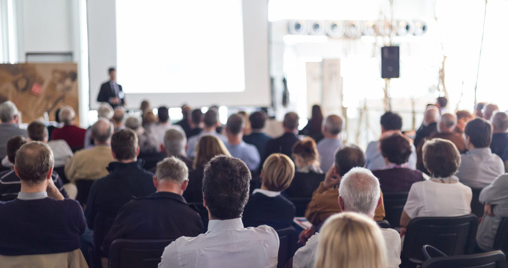 Speaker giving a talk in conference hall at business event. Audience at the conference hall. Business and Entrepreneurship concept. Focus on unrecognizable man in the audience.