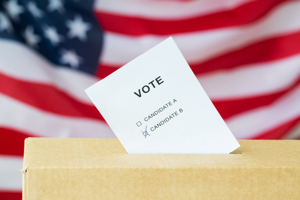 voting and civil rights concept - vote with two candidates inserted into ballot box slot on election over american flag