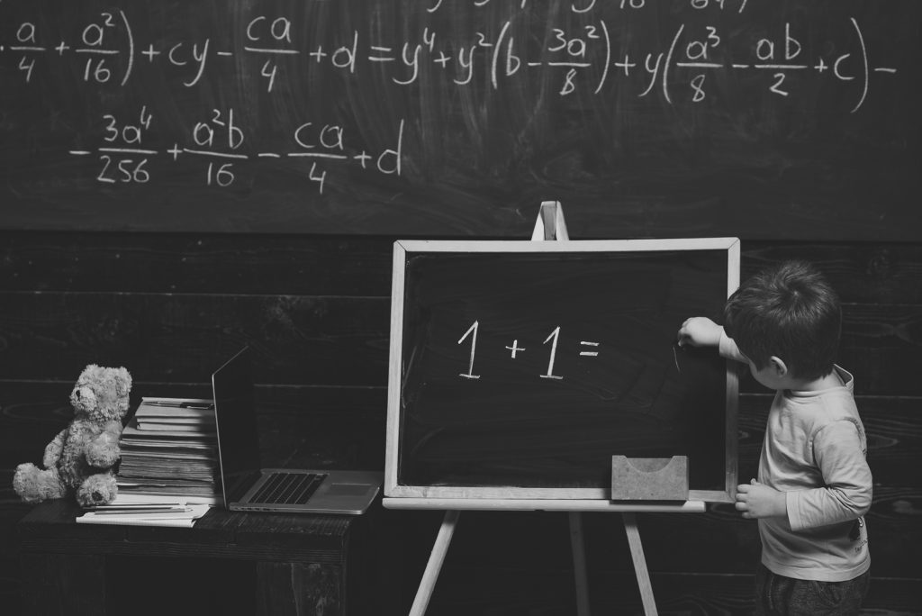 Education concept. Little boy solving equation on chalkboard. Preschool training for smart kid.