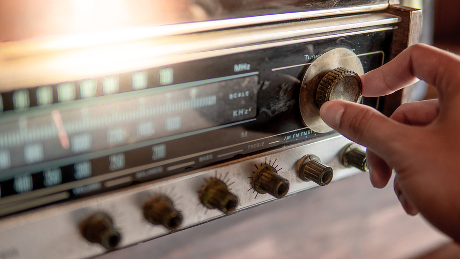 Male hand turning retro radio button. Listen to music or news with old classic radio receiver. Vintage lifestyle